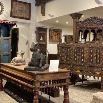 This is a photo of a well lit part of our permanent gallery space. In frame is a variety of furniture both natural and painted, deity figures, architectural pieces and more.