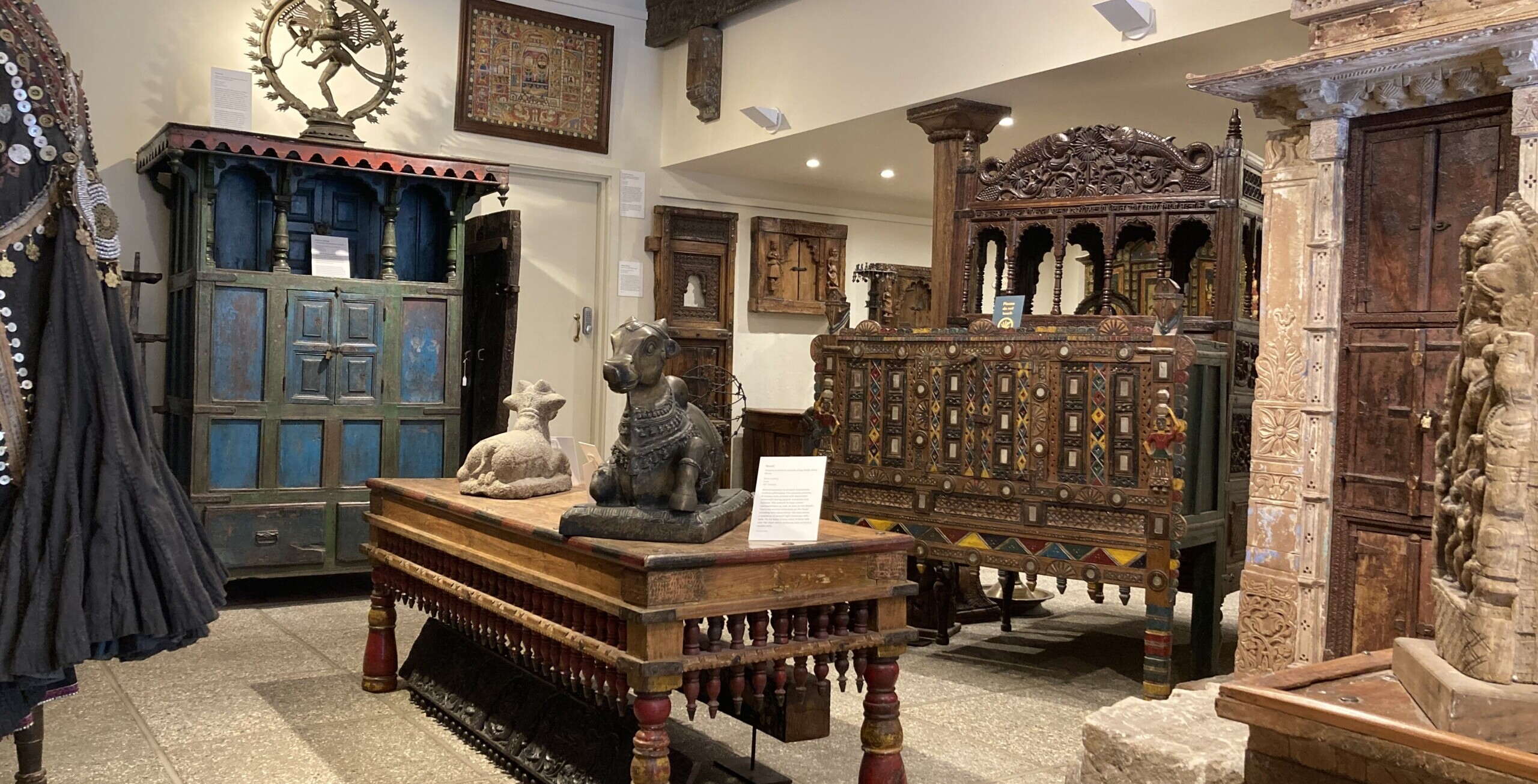 This is a photo of a well lit part of our permanent gallery space. In frame is a variety of furniture both natural and painted, deity figures, architectural pieces and more.