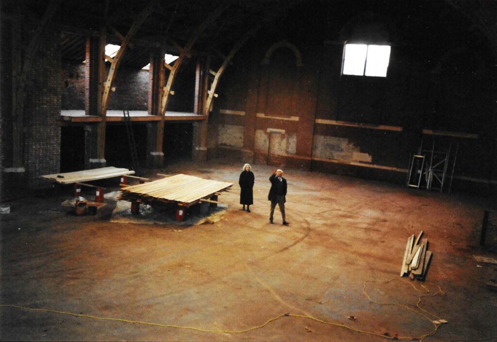 A film photo showing the empty skating rink with a man and a woman in the centre and a table next to them.