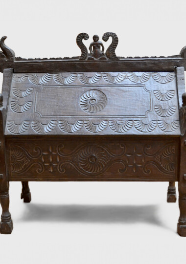 This shows a dark wood chest with short thin legs and ornate features and carving throughout.