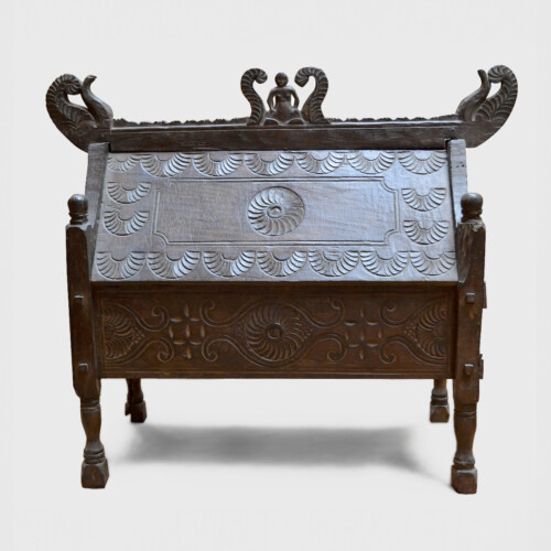 This shows a dark wood chest with short thin legs and ornate features and carving throughout.