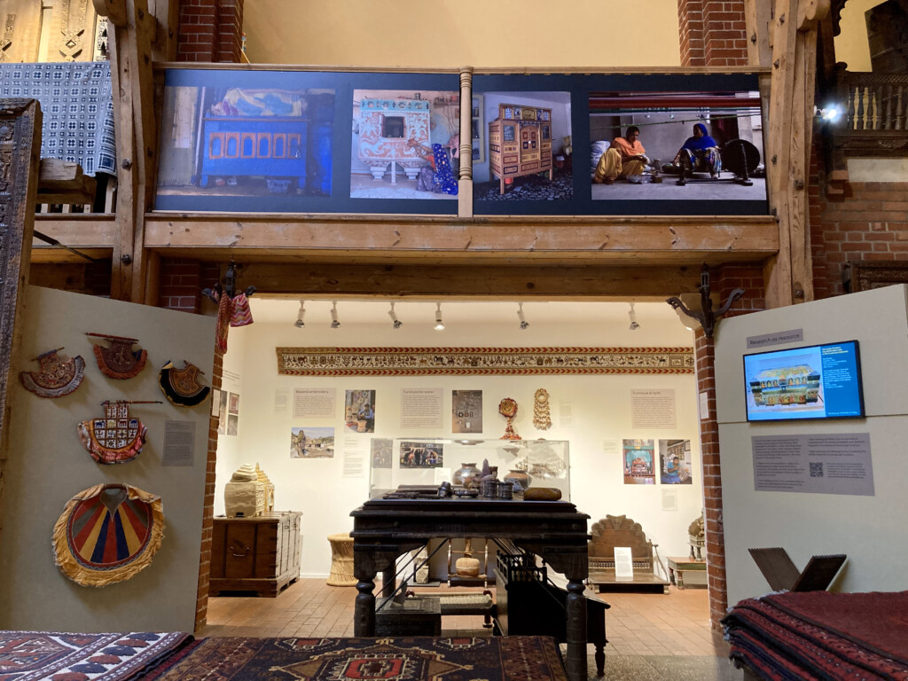 Part of our museum space showing a temporary exhibition. There are walls with various colourful objects on as well as interpretation vinyls and graphics. There are big picture graphics placed above on the banister showing furniture.