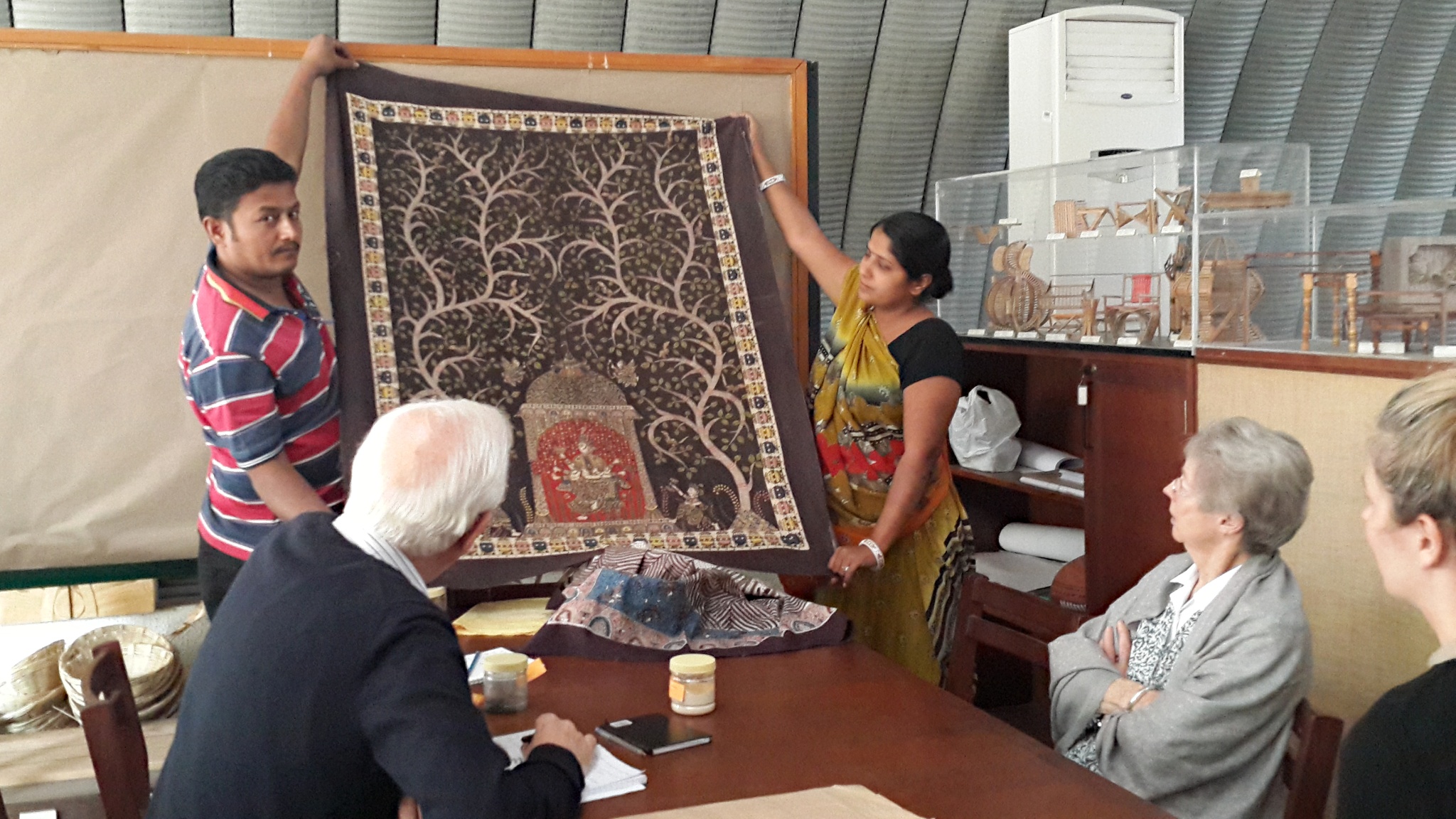 A picture of our trustees being shown a painted textile by artisans
